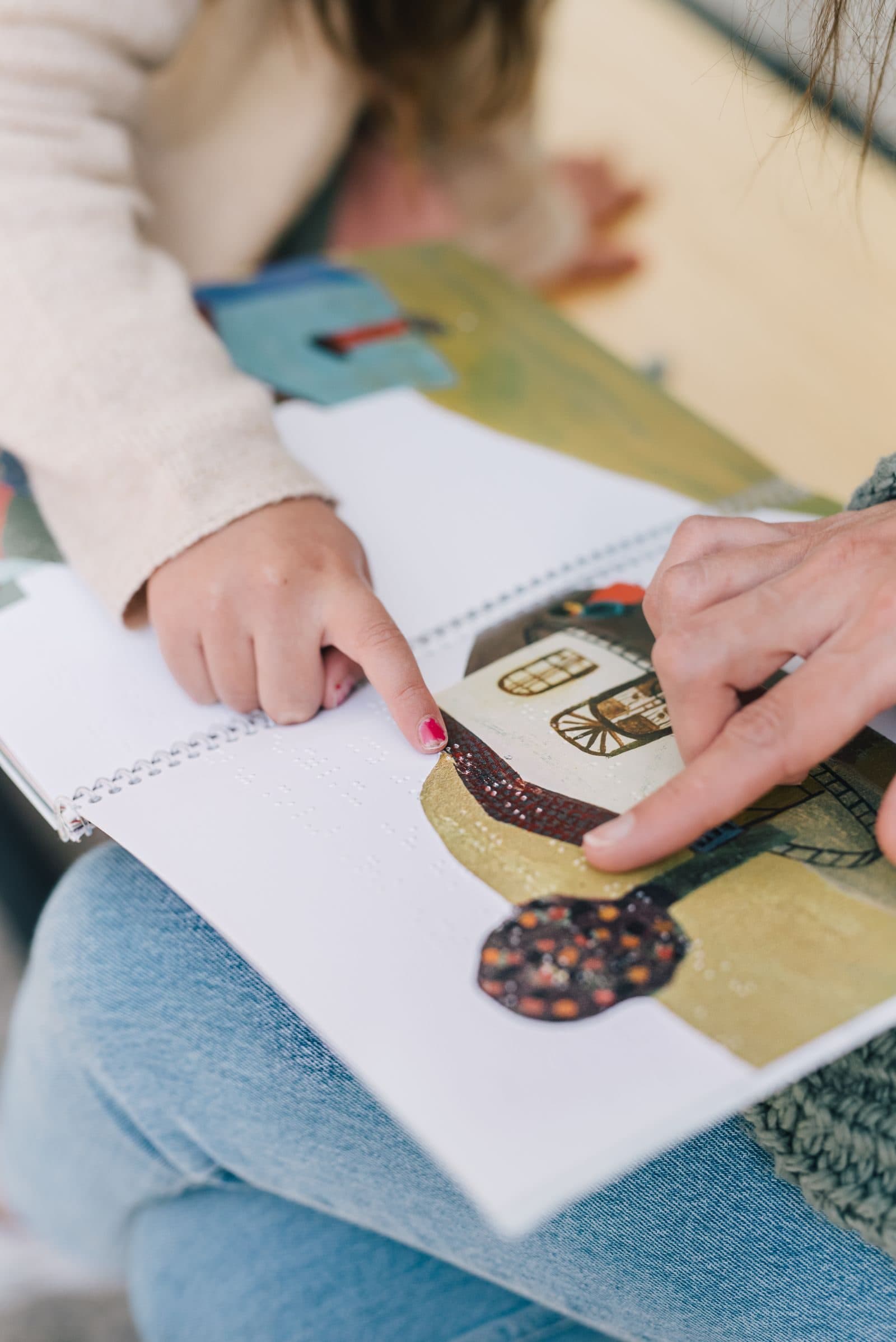 Mãos de um adulto e de uma criança apontando juntas para uma figura num livro